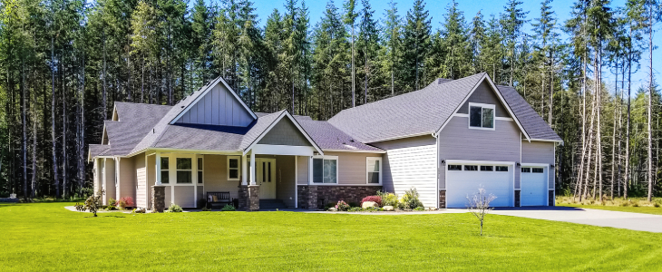 Photo of an upscale suburban home on a large lot, surrounded by forest trees on a bright summer day