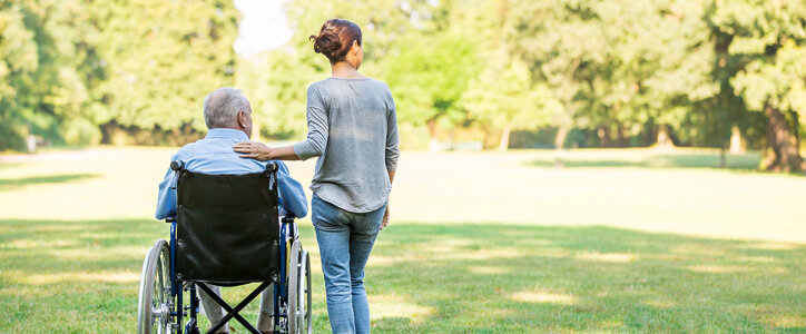 Senior man sitting on a wheelchair with caregiver next to him
