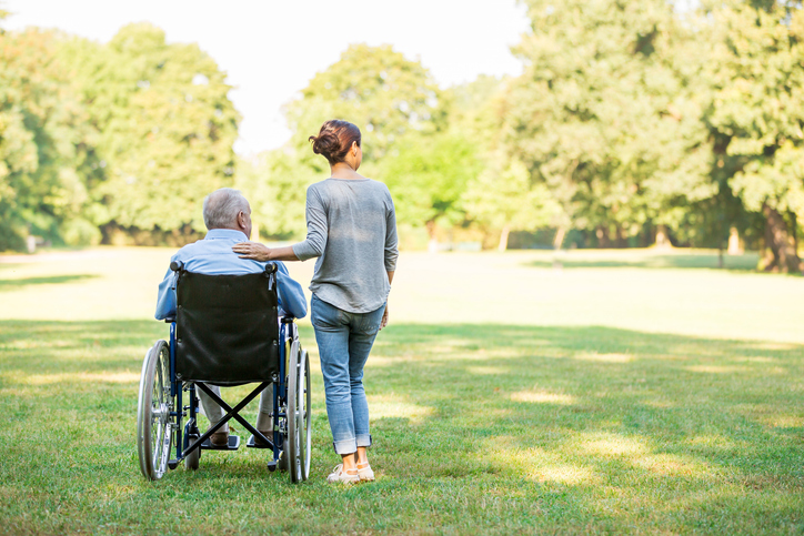 Senior man sitting on a wheelchair with caregiver next to him
